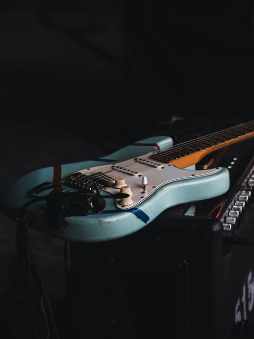 Eine blau-weiße E-Gitarre liegt auf einem Verstärker.