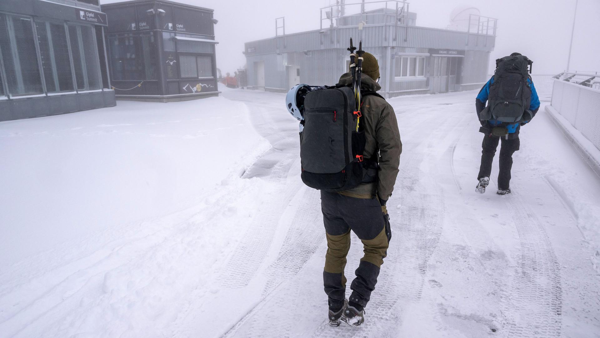 Zwei Bergsteiger laufen bei Schneefall über die Aufsichtsplattform der Zugspitze.