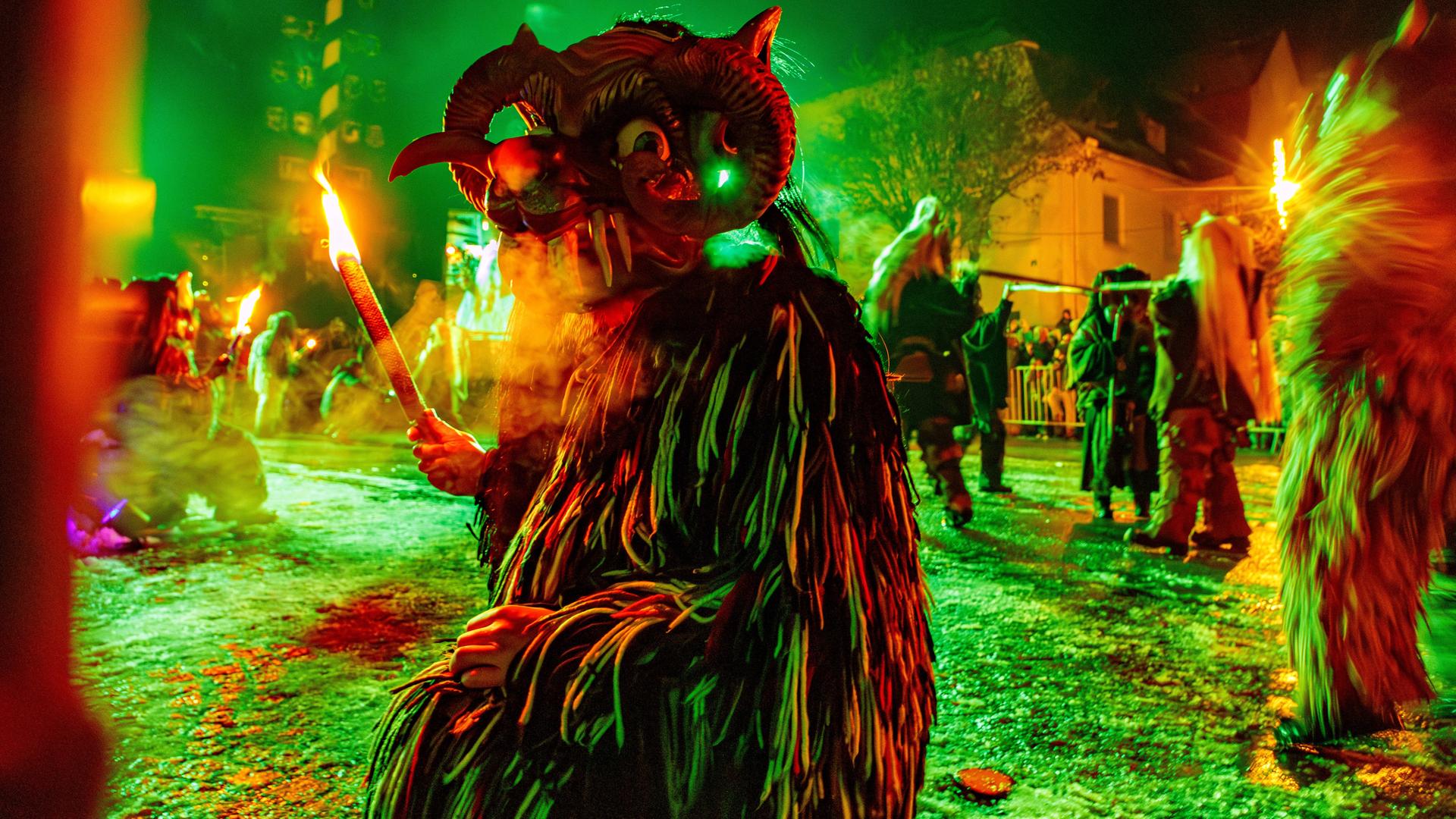 Kostümierte Person mit Maske und Fackel beim Kirchseeoner Perchten in Oberbayern