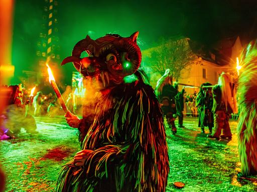Kostümierte Person mit Maske und Fackel beim Kirchseeoner Perchten in Oberbayern Kostümierte Person mit Maske und Fackel beim Kirchseeoner Perchten in Oberbayern