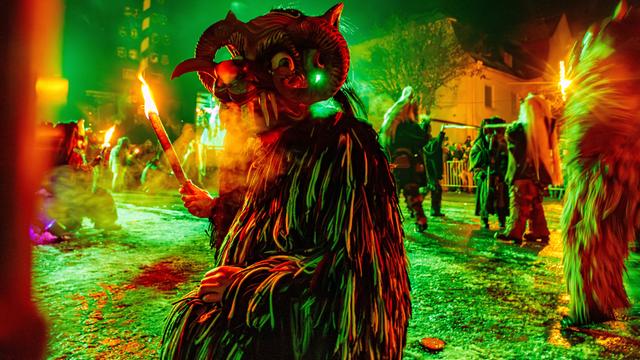 Kostümierte Person mit Maske und Fackel beim Kirchseeoner Perchten in Oberbayern