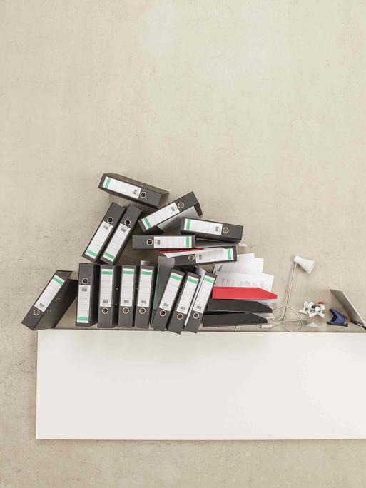Auf einem Schreibtisch stapeln sich Aktenordner