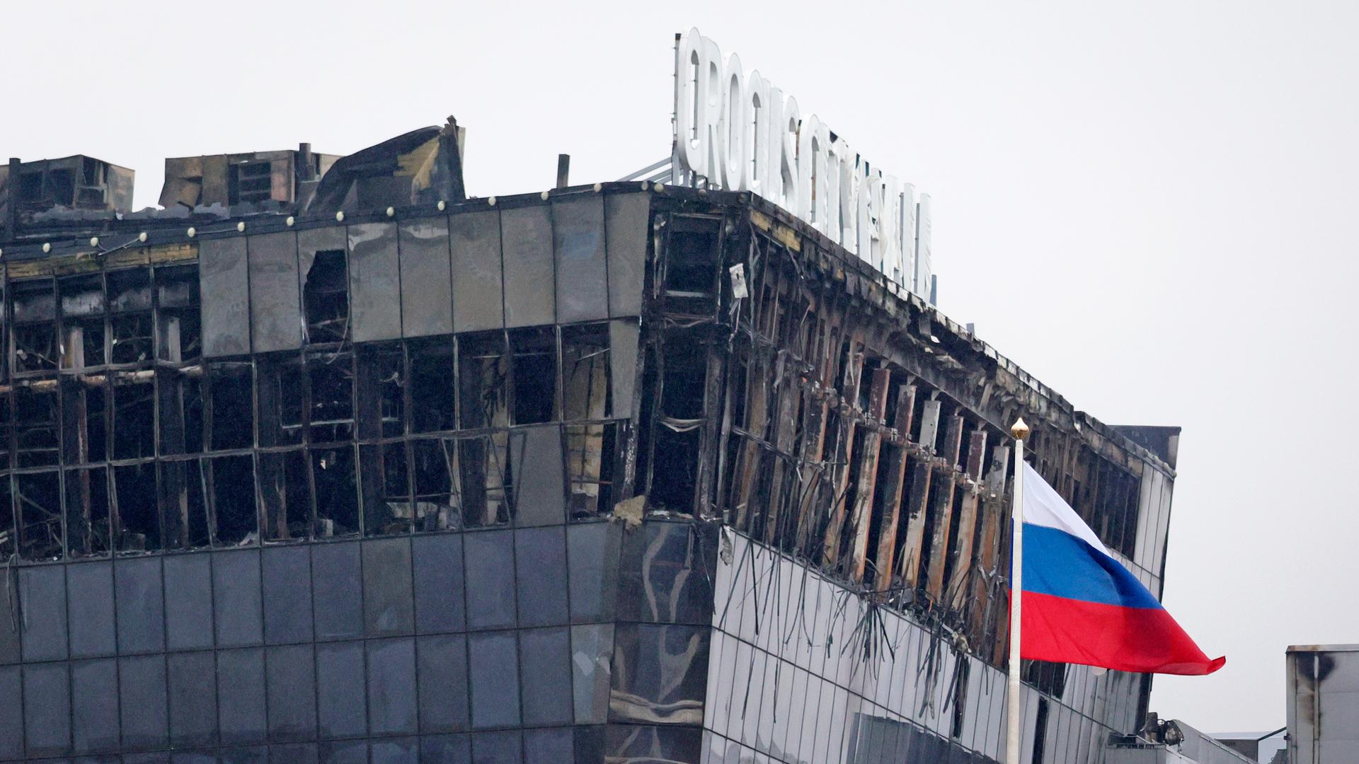 Blick auf das zerstörte Gebäude in Moskau. Die Glasfassade ist durch den Brand schwer beschädigt. Im Vordergrund weht eine russische Fahne.