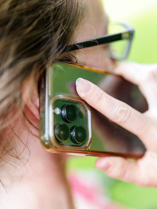 Eine junge Frau steht in einem Garten und telefoniert mit ihrem Smartphone.