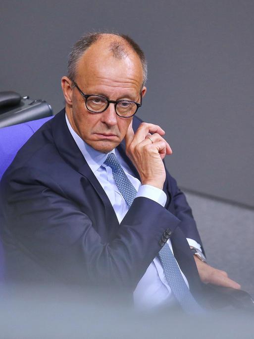 Bundeskanzler Friedrich Merz sitzt während der 25. Bundestagssitzung im Bundestag und fasst sich mit der rechten Hand hinter das linke Ohr.