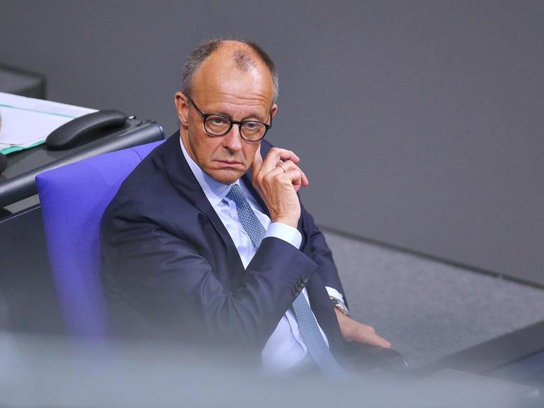 Bundeskanzler Friedrich Merz sitzt während der 25. Bundestagssitzung im Bundestag und fasst sich mit der rechten Hand hinter das linke Ohr.