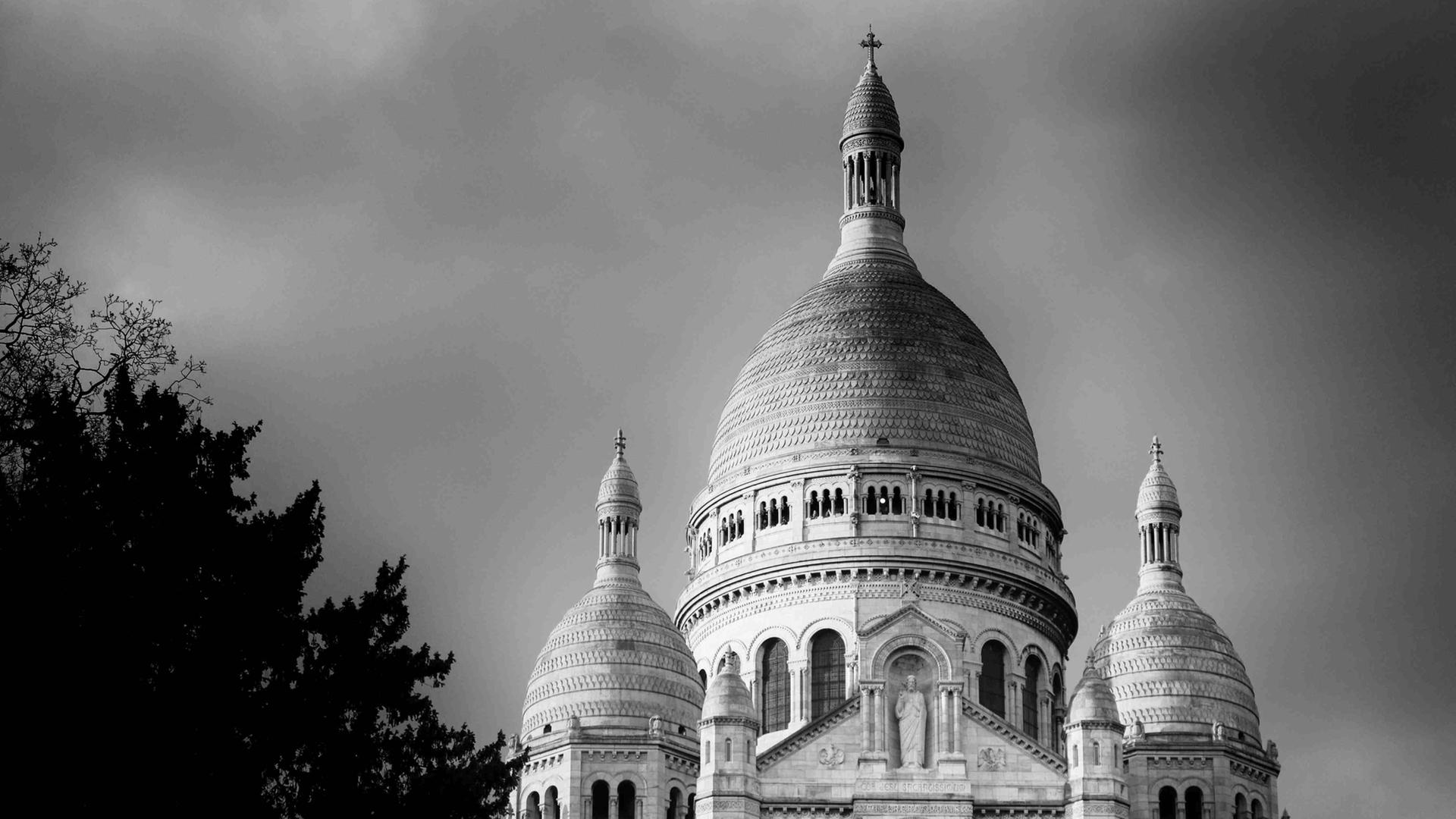 Schwarz-Weiß-Fotografie der Basilika Sacré-Coeur in Paris, leicht untersichtig, halb von einem Baum verdeckt. Schwarz-Weiß-Fotografie der Basilika Sacré-Coeur in Paris, leicht untersichtig, halb von einem Baum verdeckt.