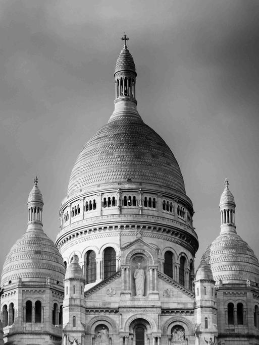 Schwarz-Weiß-Fotografie der Basilika Sacré-Coeur in Paris, leicht untersichtig, halb von einem Baum verdeckt.
