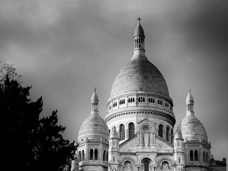 Schwarz-Weiß-Fotografie der Basilika Sacré-Coeur in Paris, leicht untersichtig, halb von einem Baum verdeckt.