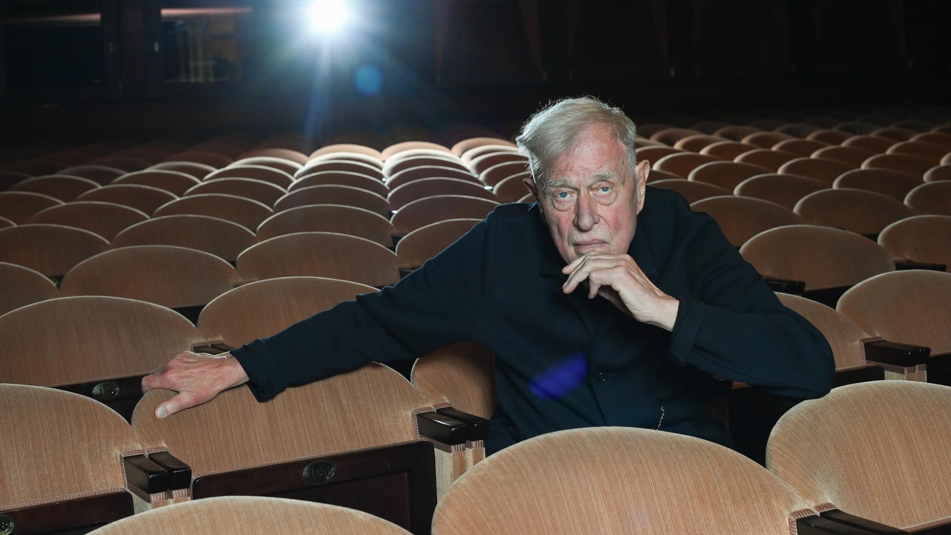 Der Theaterregisseur und Intendant Claus Peymann sitzt allein auf den Rängen im Renaissance Theater und blickt in die Kamera. 