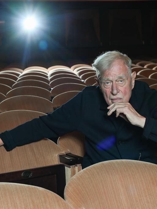 Der Theaterregisseur und Intendant Claus Peymann sitzt allein auf den Rängen im Renaissance Theater und blickt in die Kamera. 