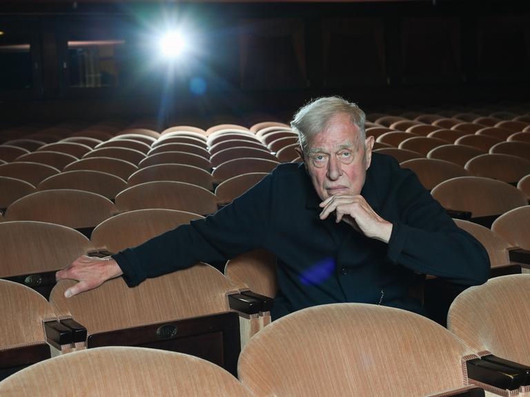 Der Theaterregisseur und Intendant Claus Peymann sitzt allein auf den Rängen im Renaissance Theater und blickt in die Kamera. 