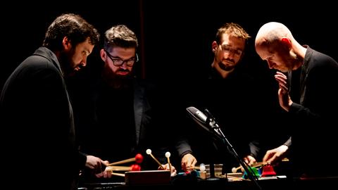 Die vier Musiker von Sō Percussion spielen im Scheinwerferlicht auf der Bühne eng zusammen an einem Instrument