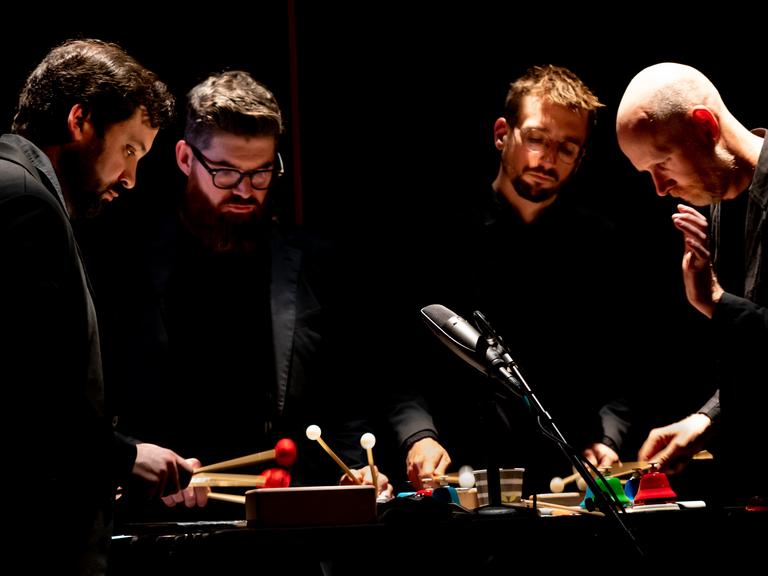 Die vier Musiker von Sō Percussion spielen im Scheinwerferlicht auf der Bühne eng zusammen an einem Instrument