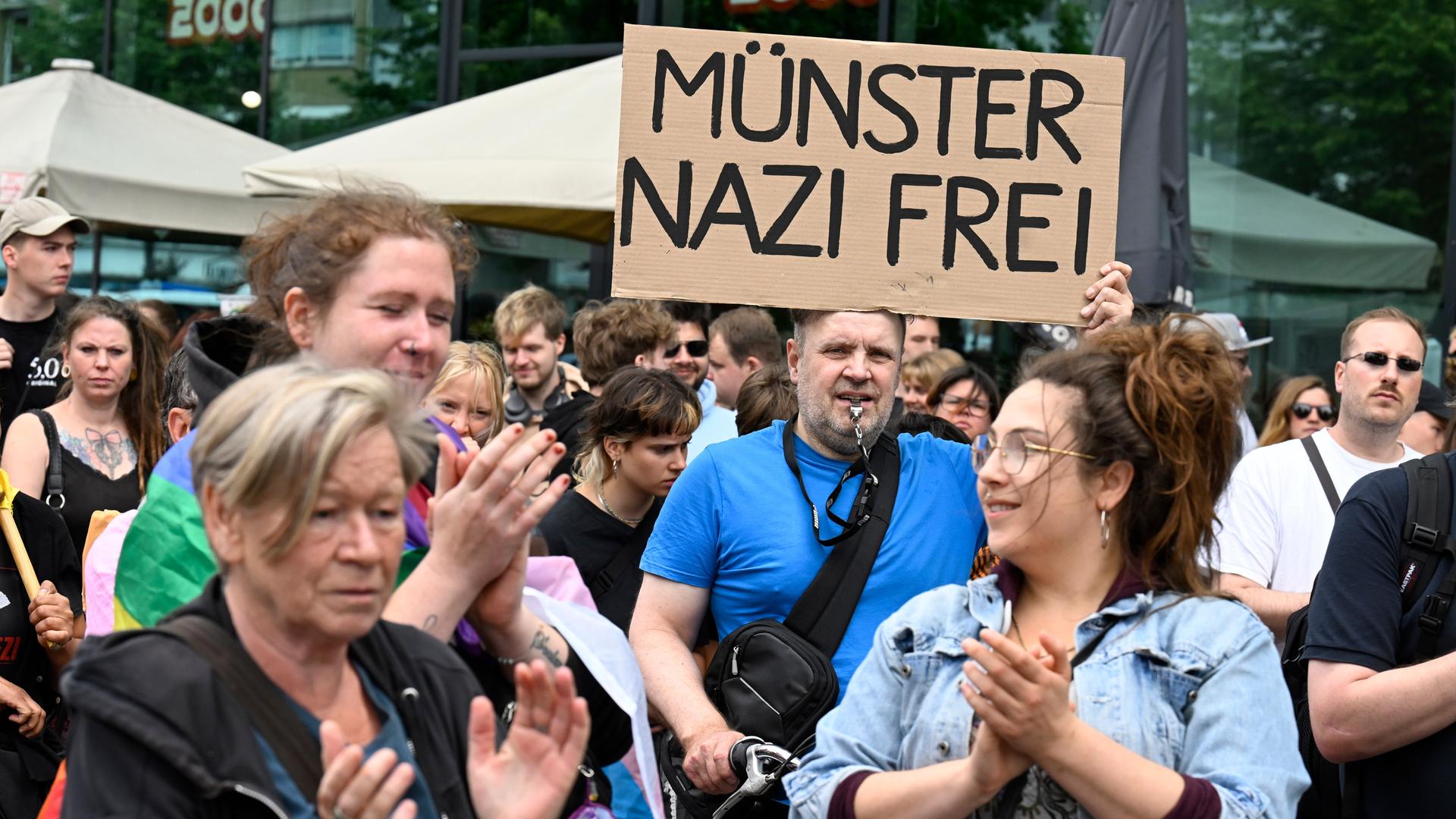 Das Bild zeigt zahlreiche der Demonstratinnen und Demonstranten. Ein Mann hält ein Pappschild hoch mit der Aufschrift "Münster Nazi-Frei".