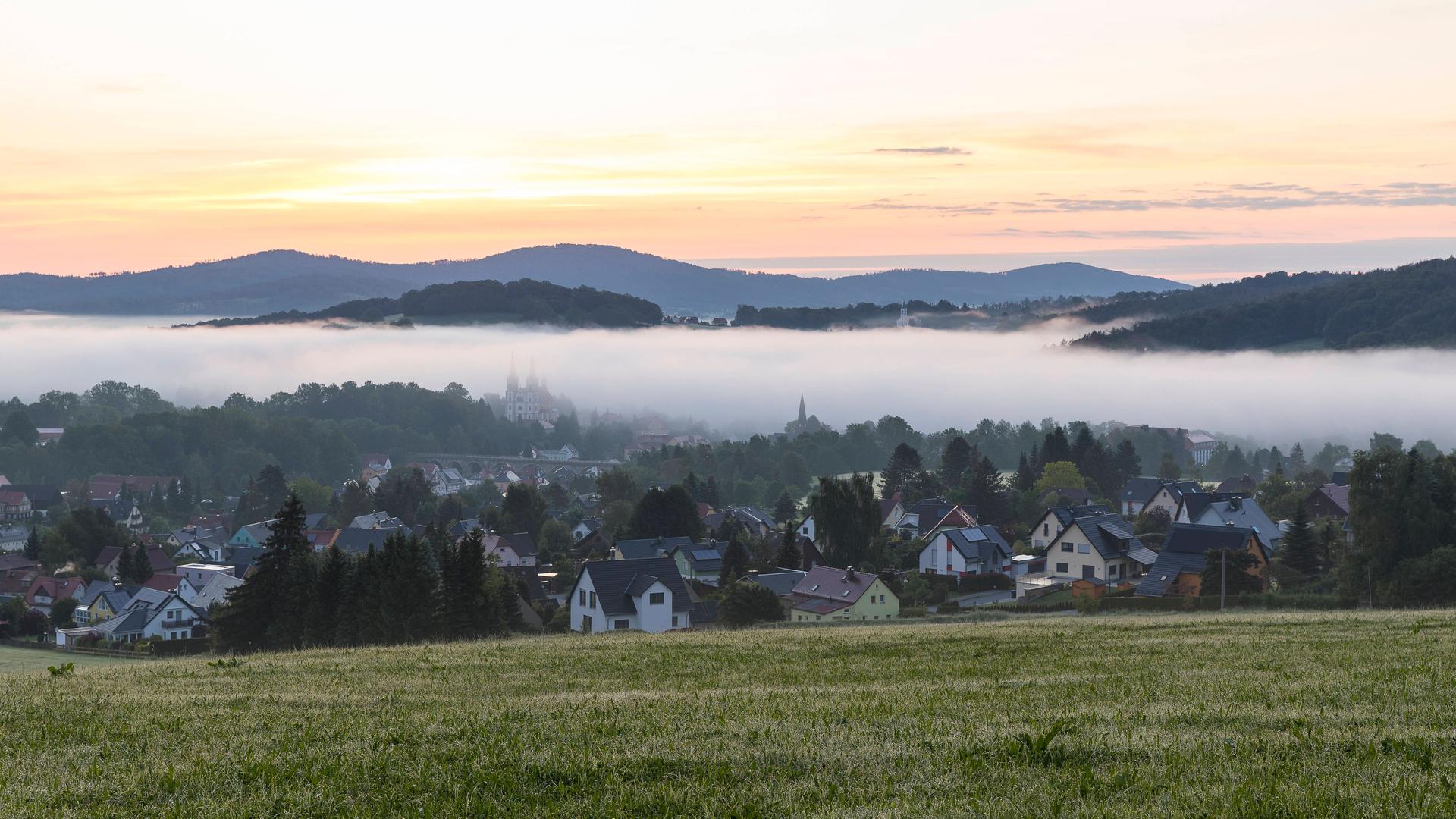 Ortsansicht mit Kirche St. Mariä Himmelfahrt im Morgennebel noch vor Sonnenaufgang, Schirgiswalde, Oberlausitzer Bergland, Sachsen.