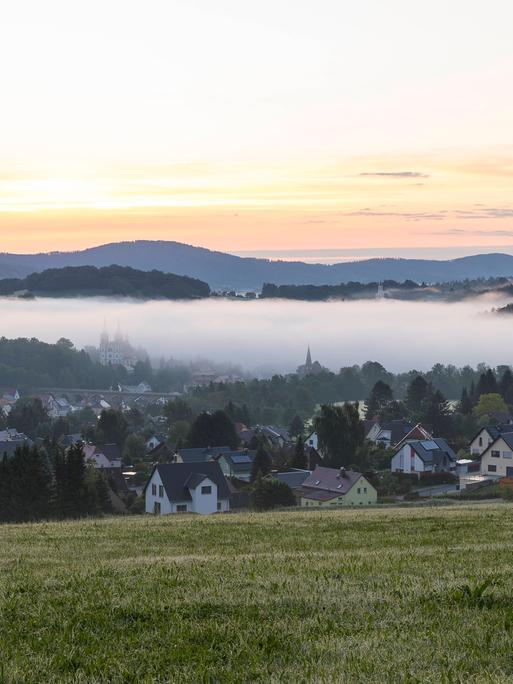 Ortsansicht mit Kirche St. Mariä Himmelfahrt im Morgennebel noch vor Sonnenaufgang, Schirgiswalde, Oberlausitzer Bergland, Sachsen.