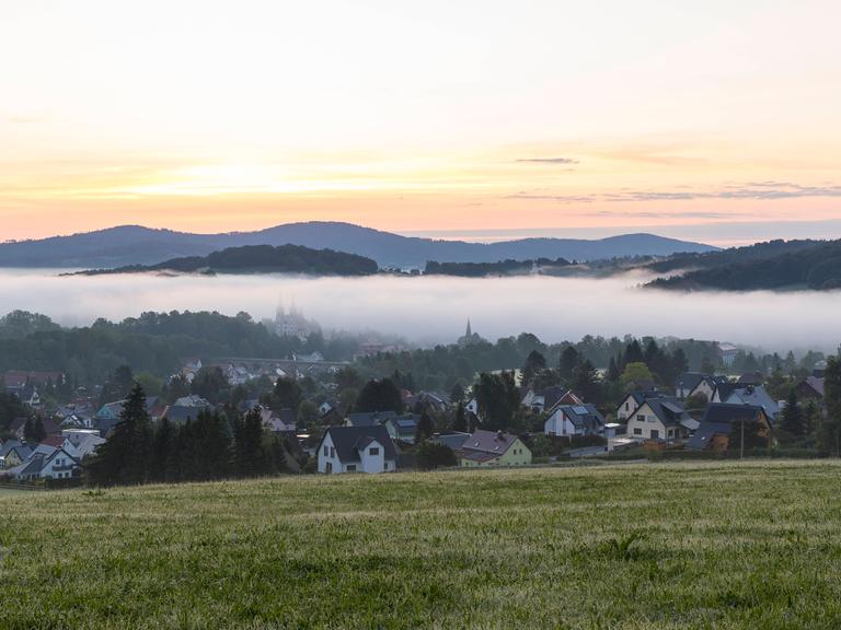 Ortsansicht mit Kirche St. Mariä Himmelfahrt im Morgennebel noch vor Sonnenaufgang, Schirgiswalde, Oberlausitzer Bergland, Sachsen.