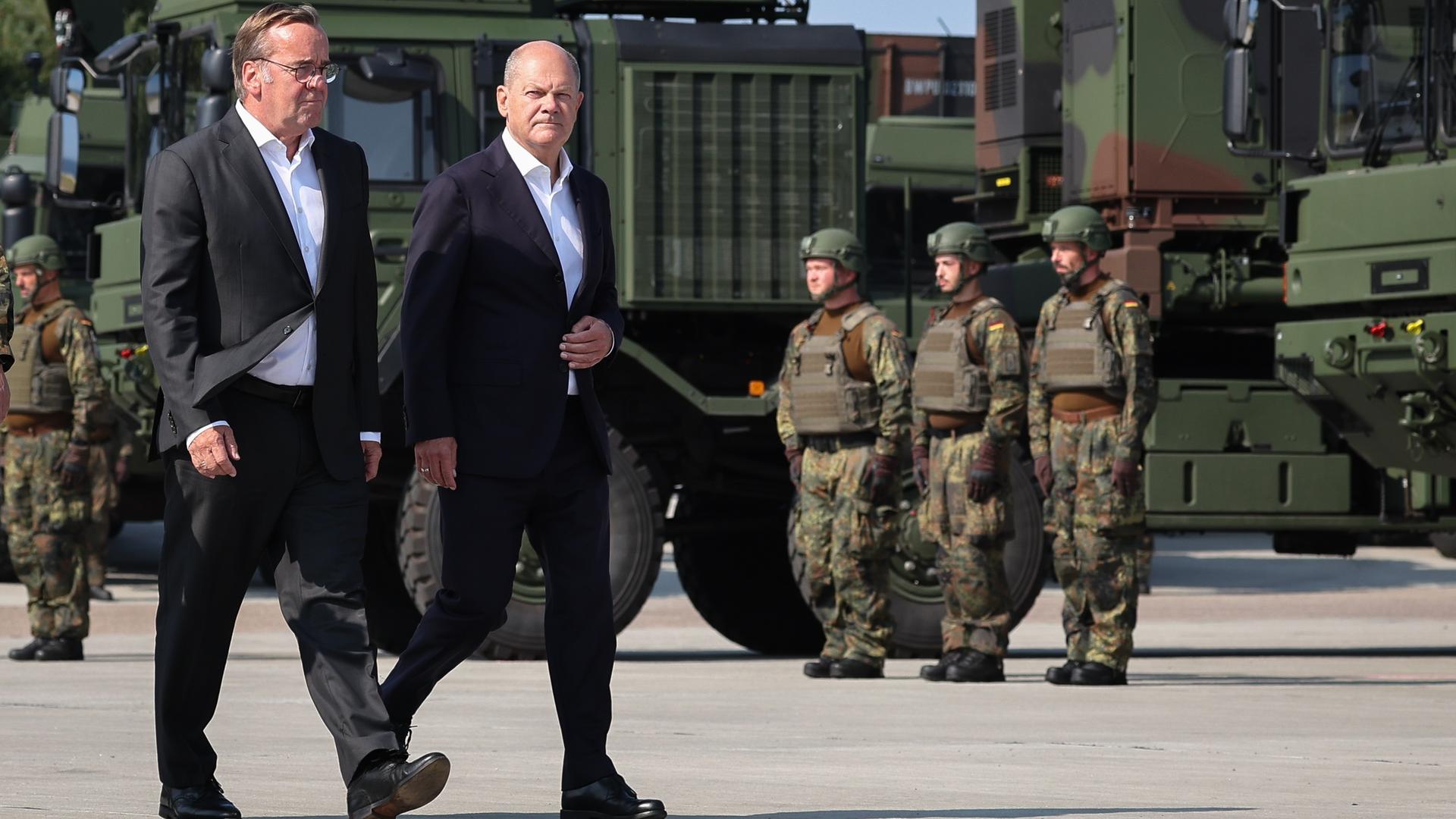 Bundeskanzler Olaf Scholz (r, SPD) und Boris Pistorius (SPD), Bundesminister der Verteidigung, laufen in Anzügen bei der feierlichen Indienststellung des Luftverteidigungssystems IRIS- T SLM in der Kaserne Todendorf.