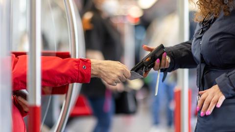 Eine Fahrkartenkontrolleurin kontrolliert mit einem elektronischen Lesegerät den Fahrschein von einem Fahrgast.