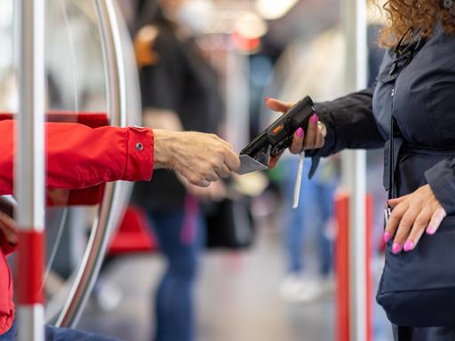 Eine Fahrkartenkontrolleurin kontrolliert mit einem elektronischen Lesegerät den Fahrschein von einem Fahrgast.