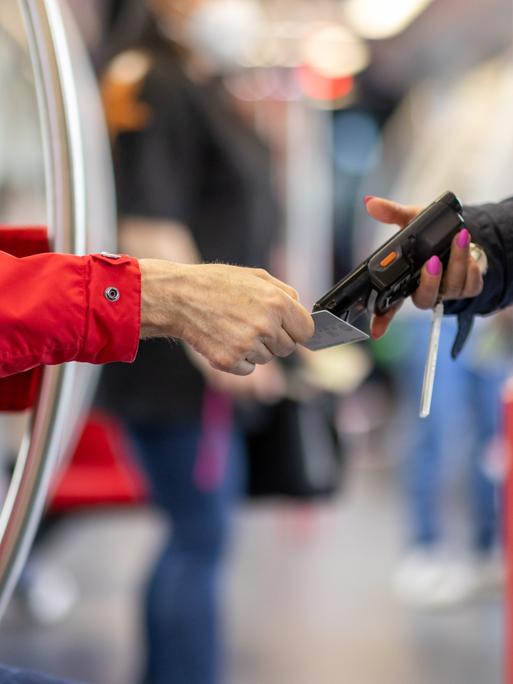 Eine Fahrkartenkontrolleurin kontrolliert mit einem elektronischen Lesegerät den Fahrschein von einem Fahrgast.