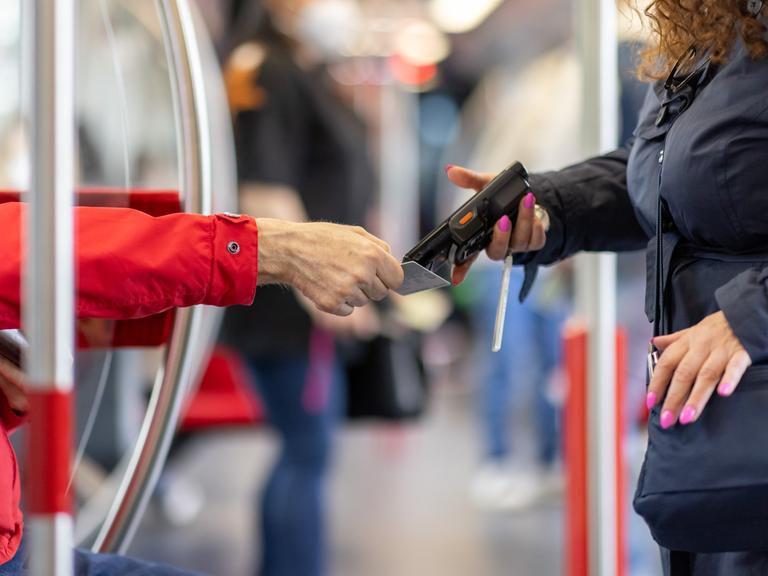 Eine Fahrkartenkontrolleurin kontrolliert mit einem elektronischen Lesegerät den Fahrschein von einem Fahrgast.