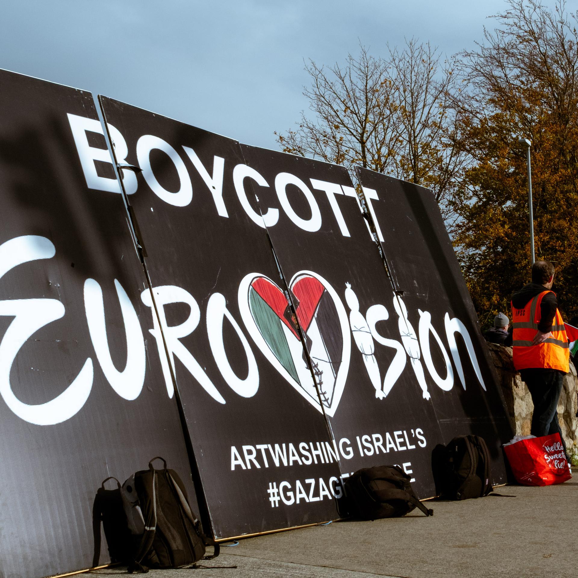 Auf einem Plakatt steht: "Boykott Eurovision". Daneben stehen einige Demonstranten.