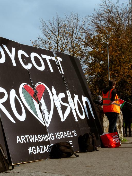 Auf einem Plakatt steht: "Boykott Eurovision". Daneben stehen einige Demonstranten.