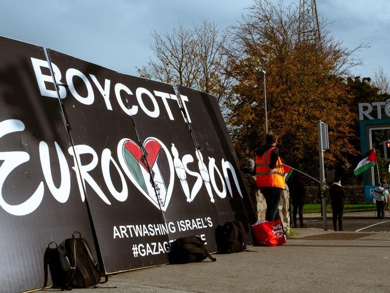 Auf einem Plakatt steht: "Boykott Eurovision". Daneben stehen einige Demonstranten.
