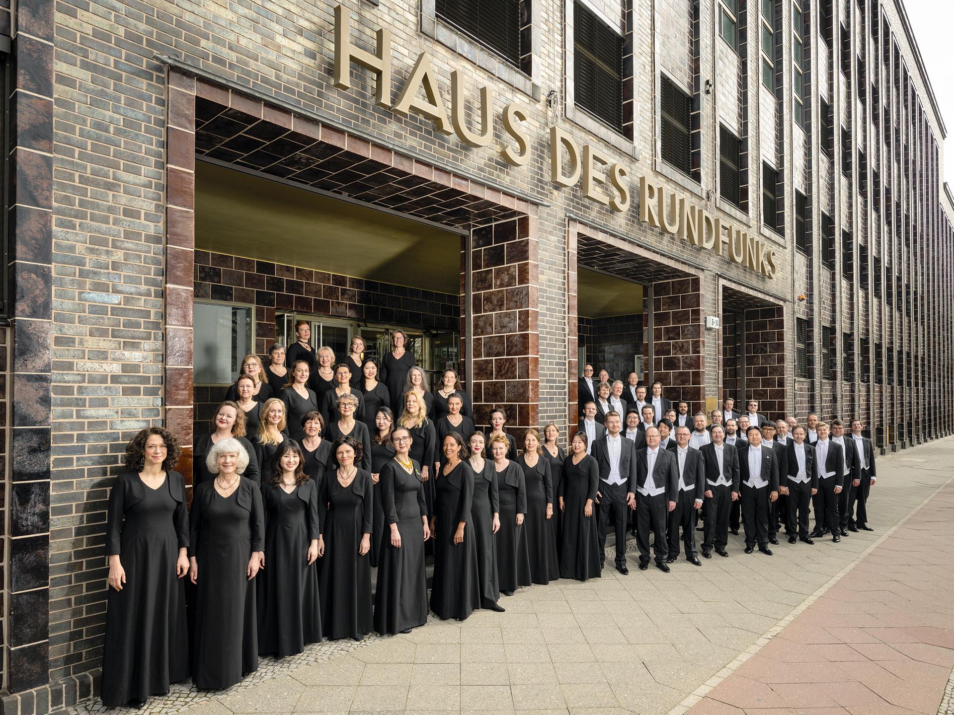 Der Chor steht vor dem historischen, braun gekachelten und unter Denkmal stehenden Gebäude, auf dem große Buchstaben zu sehen sind: "Haus des Rundfunks".