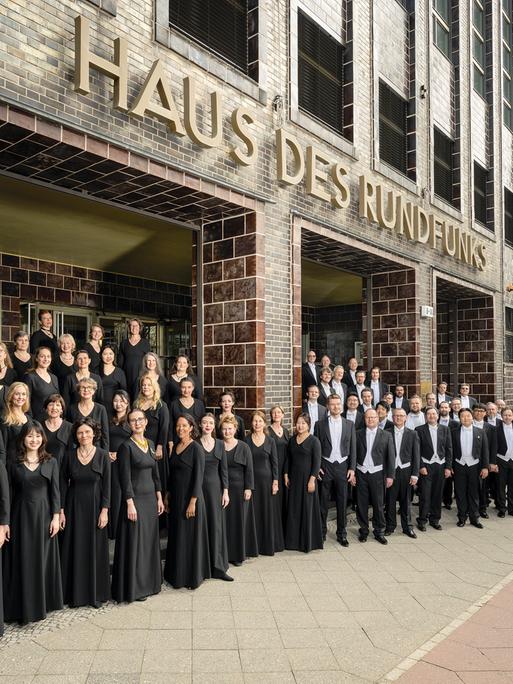 Der Chor steht vor dem historischen, braun gekachelten und unter Denkmal stehenden Gebäude, auf dem große Buchstaben zu sehen sind: "Haus des Rundfunks".