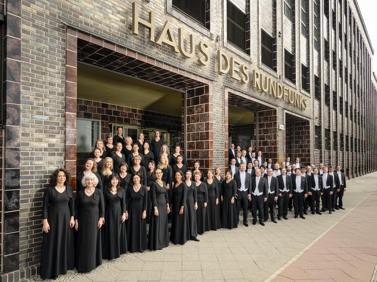 Der Chor steht vor dem historischen, braun gekachelten und unter Denkmal stehenden Gebäude, auf dem große Buchstaben zu sehen sind: "Haus des Rundfunks".