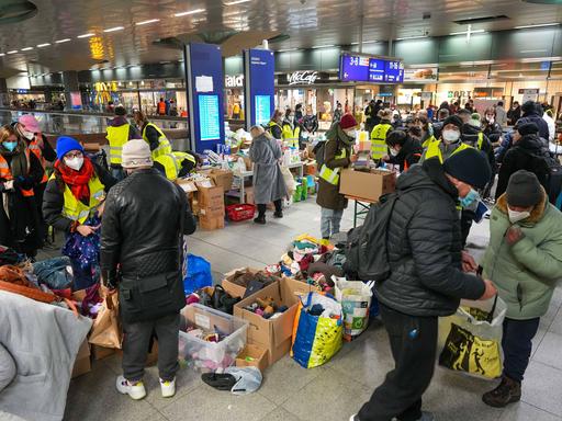 Maskierte Menschen am Bahnhof mit Kisten voller Kleidung.