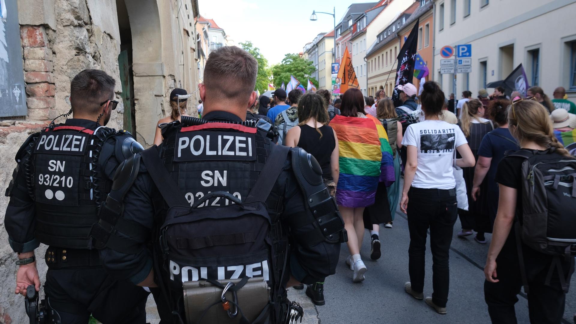 Im Vordergrund sind mehrere Polizisten zu sehen, die einen Demonstrationszug in Bautzen absichern.