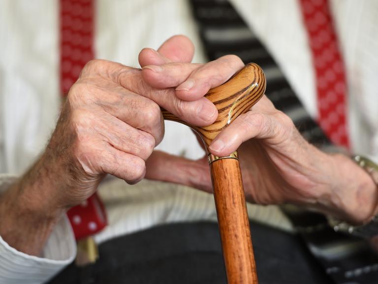 Ein älterer Parkinson-Patient, der einen Gehstock hält.