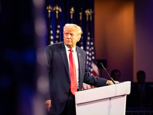 Donald Trump steht an einem Pednerpult und blickt zur Seite.