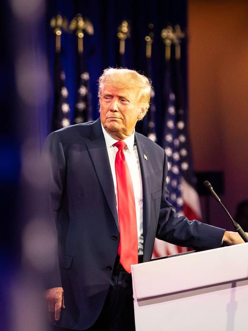 Donald Trump steht an einem Pednerpult und blickt zur Seite.