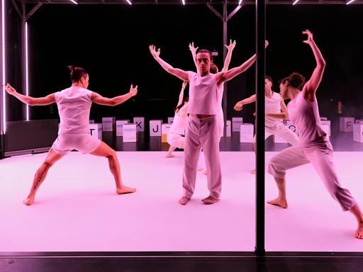 Auf einer pink beleuchteten Bühnen tanzen Personen in weißer Kleidung