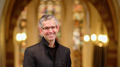 Andreas Reize steht auf einer Kirchenempore und lächelt in die Kamera.