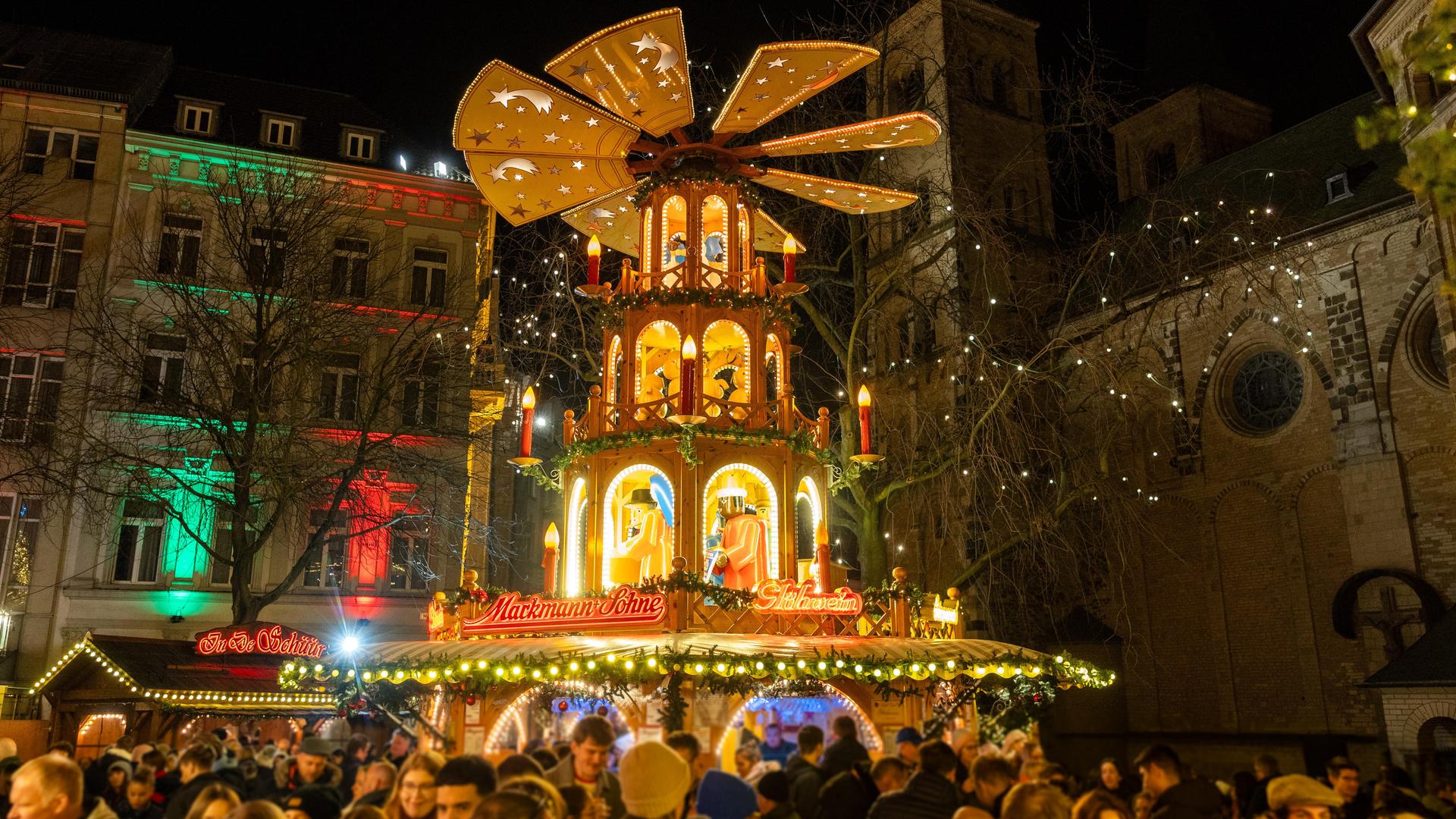 Die Weihnachtspyramide auf dem Bonner Weihnachtsmarkt steht am Abend auf dem Münsterplatz vor dem Bonner Münster. 