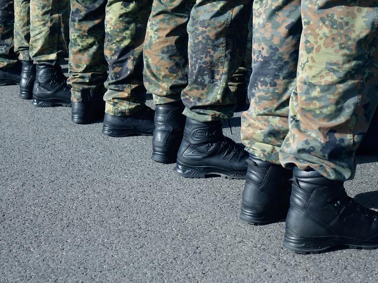 Zu sehen sind die Beine mehrerer Bundeswehrsoldaten, die in einer Reihe stehen, sie tragen Tarnkleidung. 