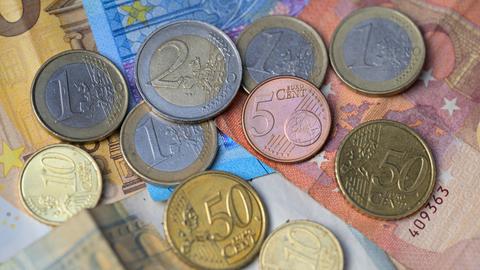 Euro-Banknoten und -Münzen liegen aufeinandergestapelt.