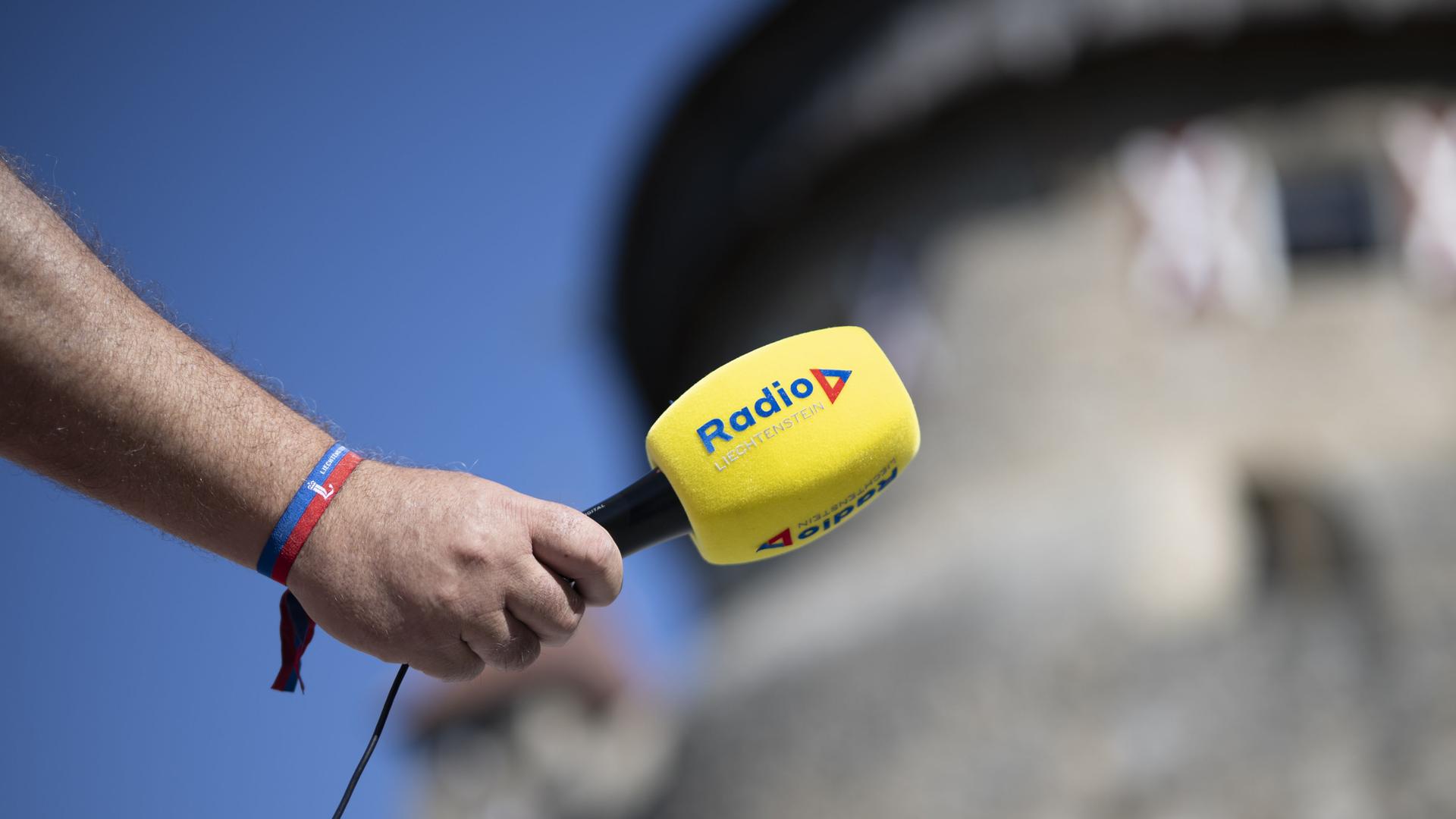 Ein gelbes Mikrofon mit dem Logo des Senders Radio Liechtenstein wird von einer Hand vor die Kamera gehalten.