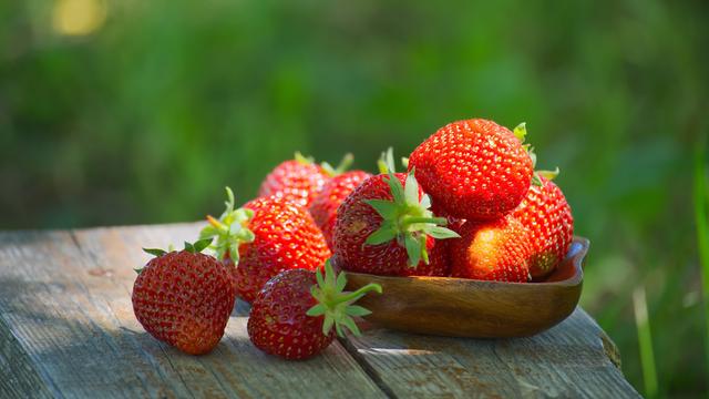 Frische Erdbeeren liegen in einer Holzschale auf einem alten Tisch in einem Garten.
