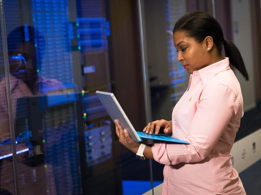 Eine Frau steht mit Laptop in der Hand in einem Rechenzentrum