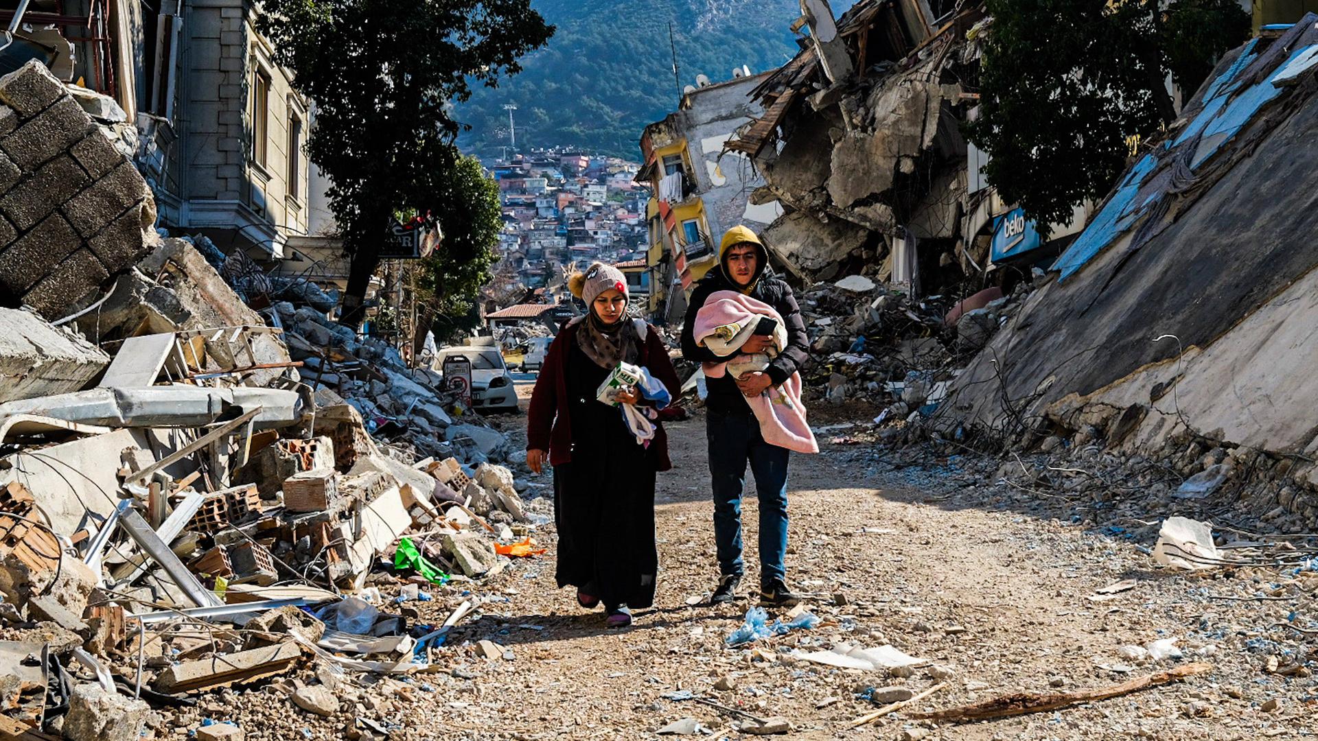 Eine Frau und ein Mann laufen im Erdbebengebiet durch die Ruinen ihrer Sadt.