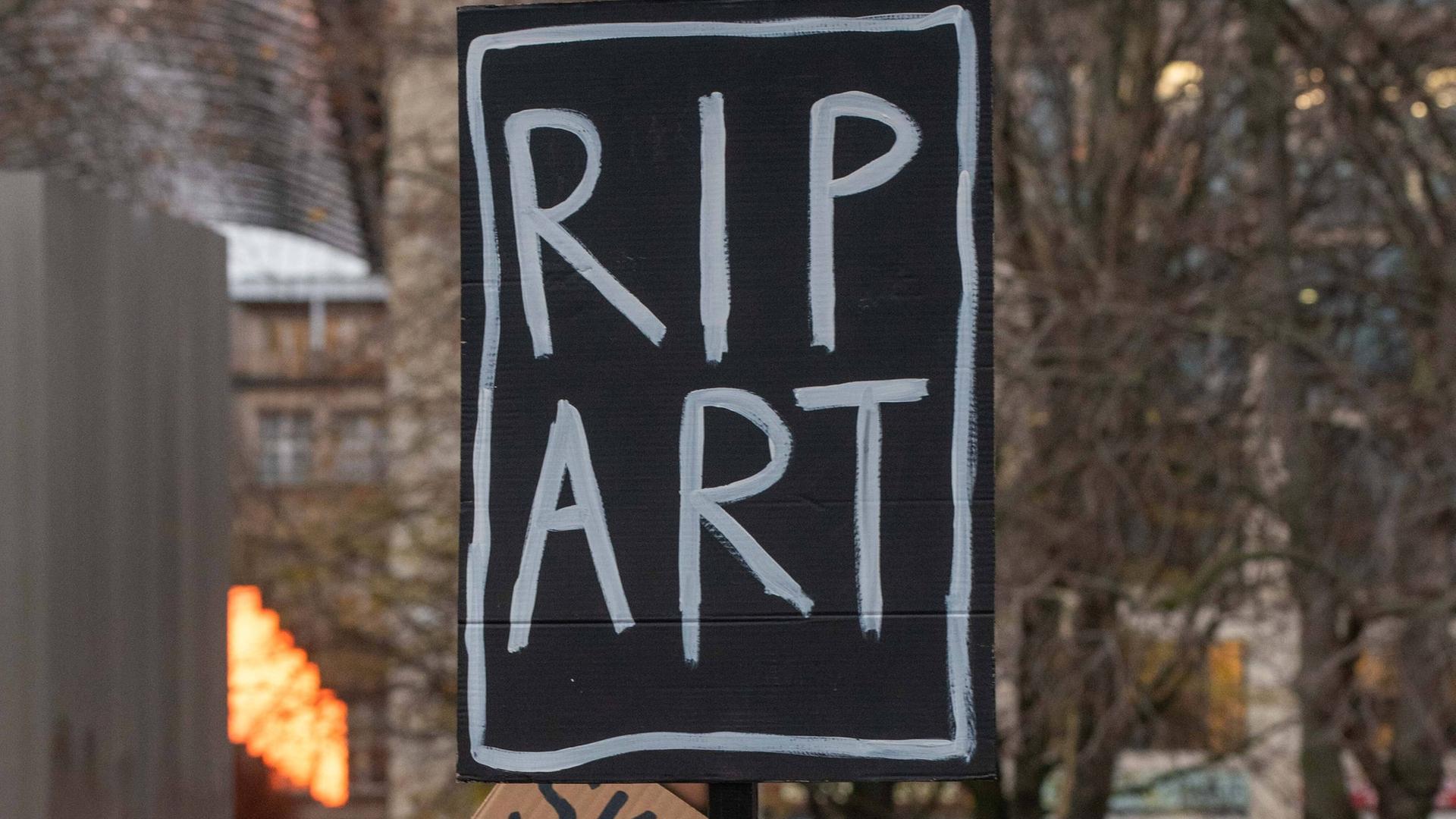 Auf einer Demo hält ein Mann ein Schild mit der Aufschrift "RIP ART" in die Luft.
