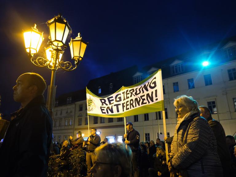 Teilnehmer einer Demonstration versammeln sich auf dem Marktplatz, im Hintergrund ein Transparent der Kleinpartei "Freie Sachsen" mit dem Schriftzug "Regierung entfernen!"