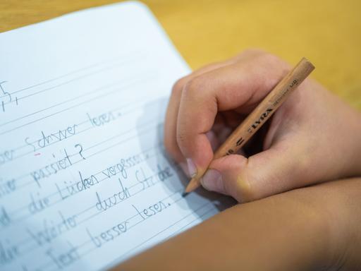 Grundschüler schreibt mit einem Bleistift auf ein Blatt.